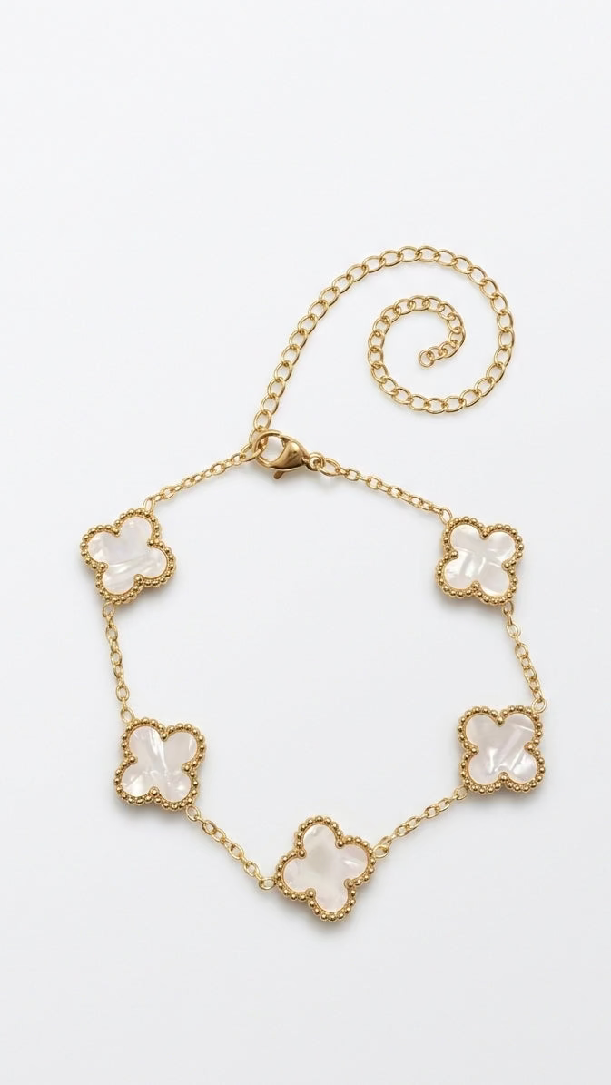 A delicate 18K gold-plated cable chain bracelet featuring white mother-of-pearl clover motifs with a beaded gold border on a person's wrist.