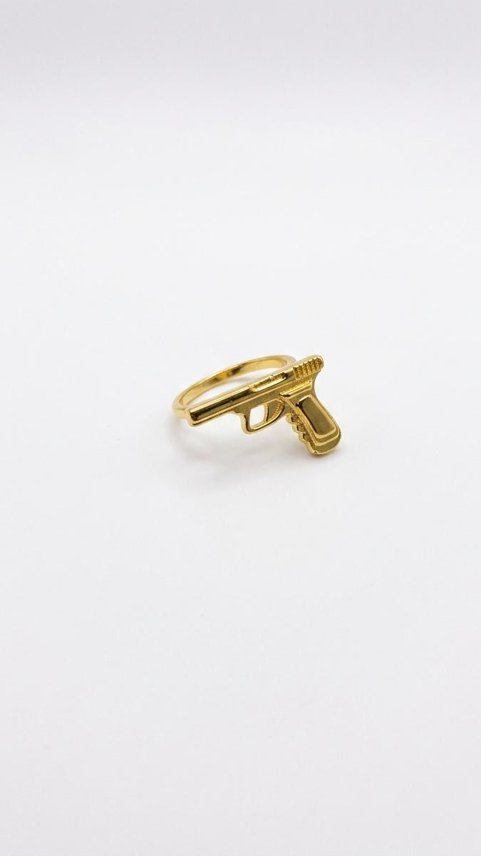 A detailed 18K gold-plated ring featuring a 3D sculpted pistol motif on a polished slim gold band.
