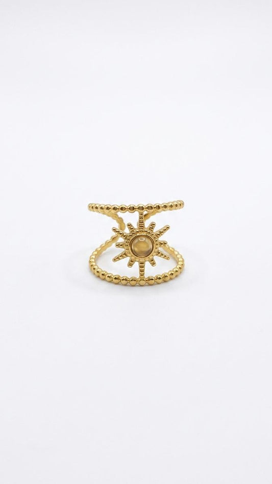 A detailed 18K gold-plated statement ring featuring a central sunburst motif between two beaded parallel bands on a white background.