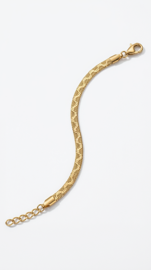 A flat 18K gold-plated herringbone bracelet with an engraved textured pattern laying flat on a model's wrist.