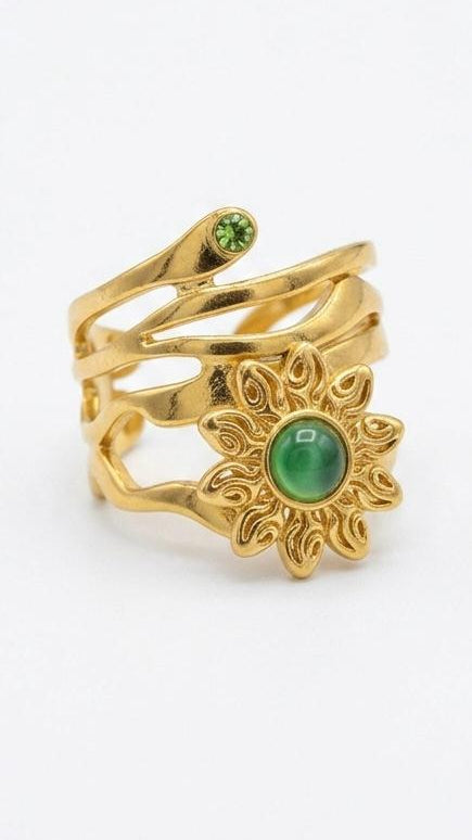 A multi-layered 18K gold-plated ring featuring an emerald-green sun motif and a serpent-inspired wrap design on a white background.