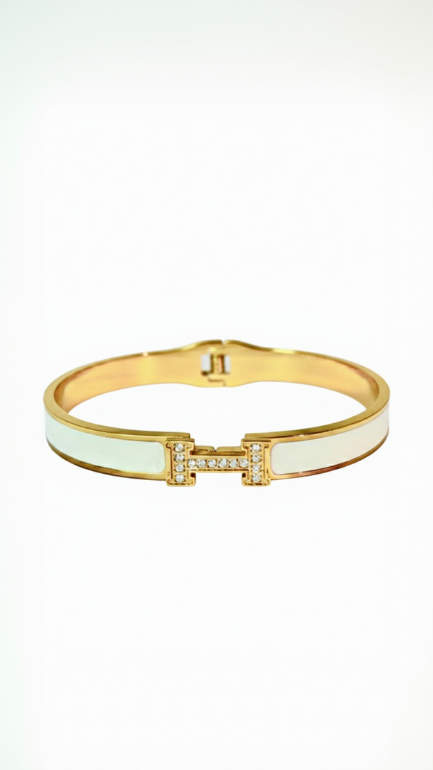 A wide 18K gold-plated bangle featuring a central H clasp and vibrant red enamel inlay on a white background.