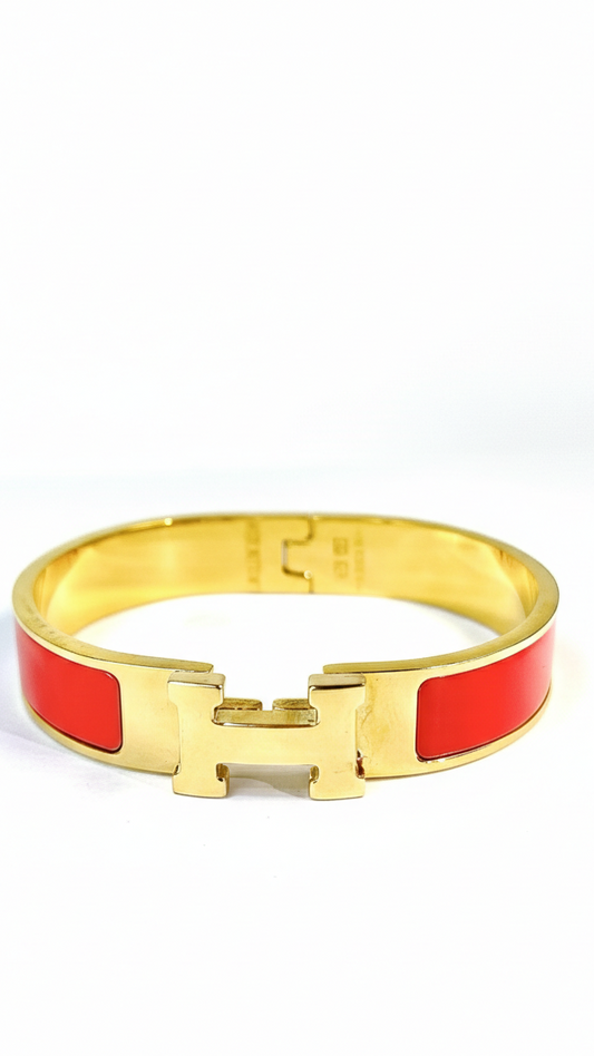 A wide 18K gold-plated bangle featuring a central crystal-encrusted H clasp and vibrant enamel inlay available in red or white.