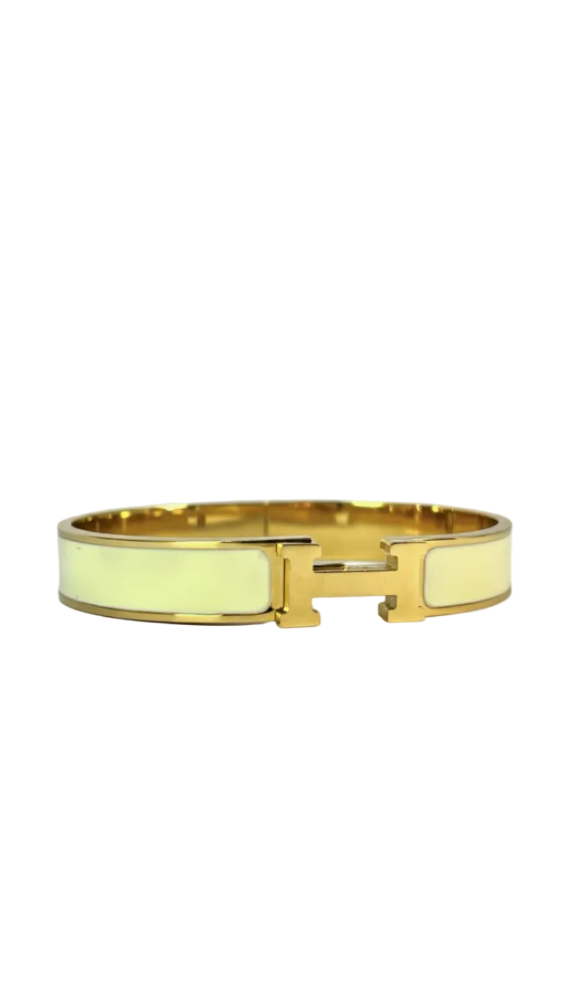 A wide 18K gold-plated bangle featuring a central gold H clasp and white enamel inlay on a white background.